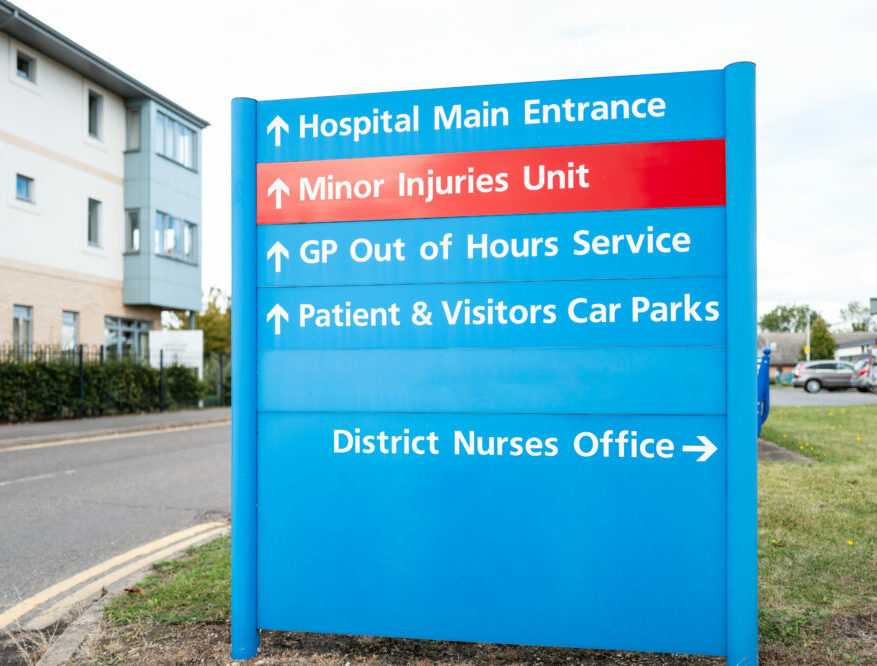 Large, NHS type information sign showing outpatients department, out of hours doctors and a minor injury unit.